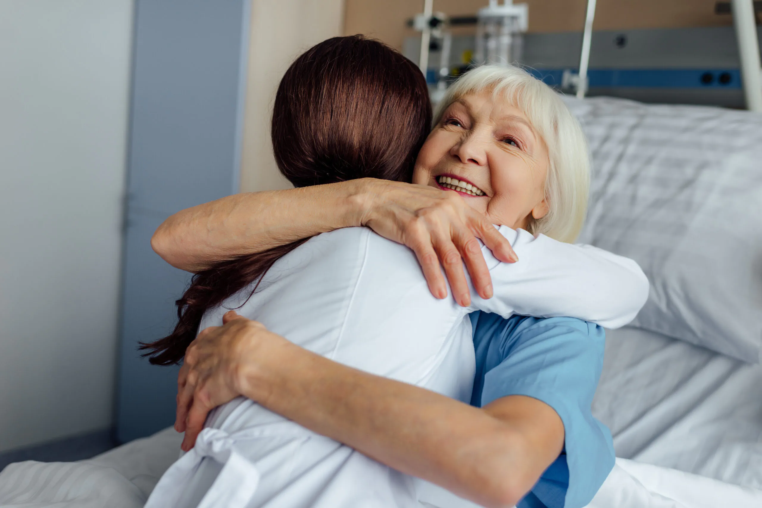 happy senior woman lying in bed and hugging female doctor in hos